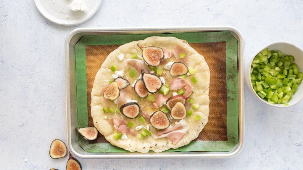 uncooked fig and prosciutto pizza on a baking sheet with ingredients on the side