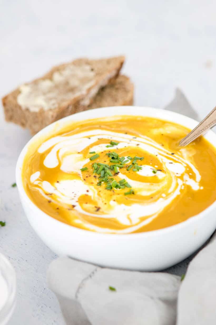 curried pumpkin soup with coconut milk swirl in a white bowl with bread in the background