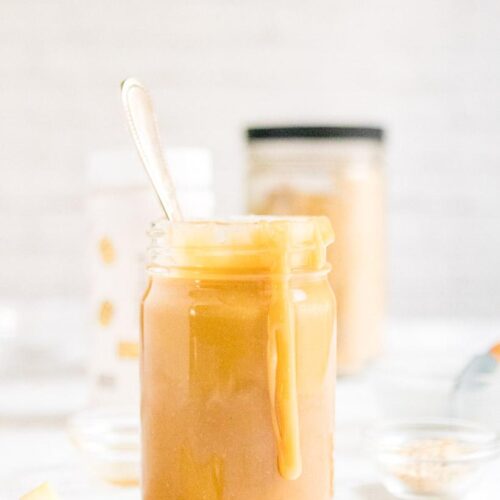 peanut butter caramel sauce on spoon with jar of caramel in background