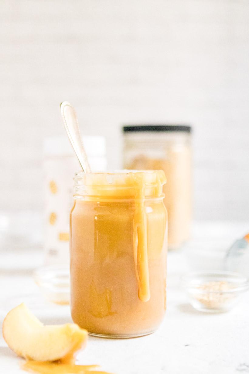 peanut butter caramel sauce on spoon with jar of caramel in background