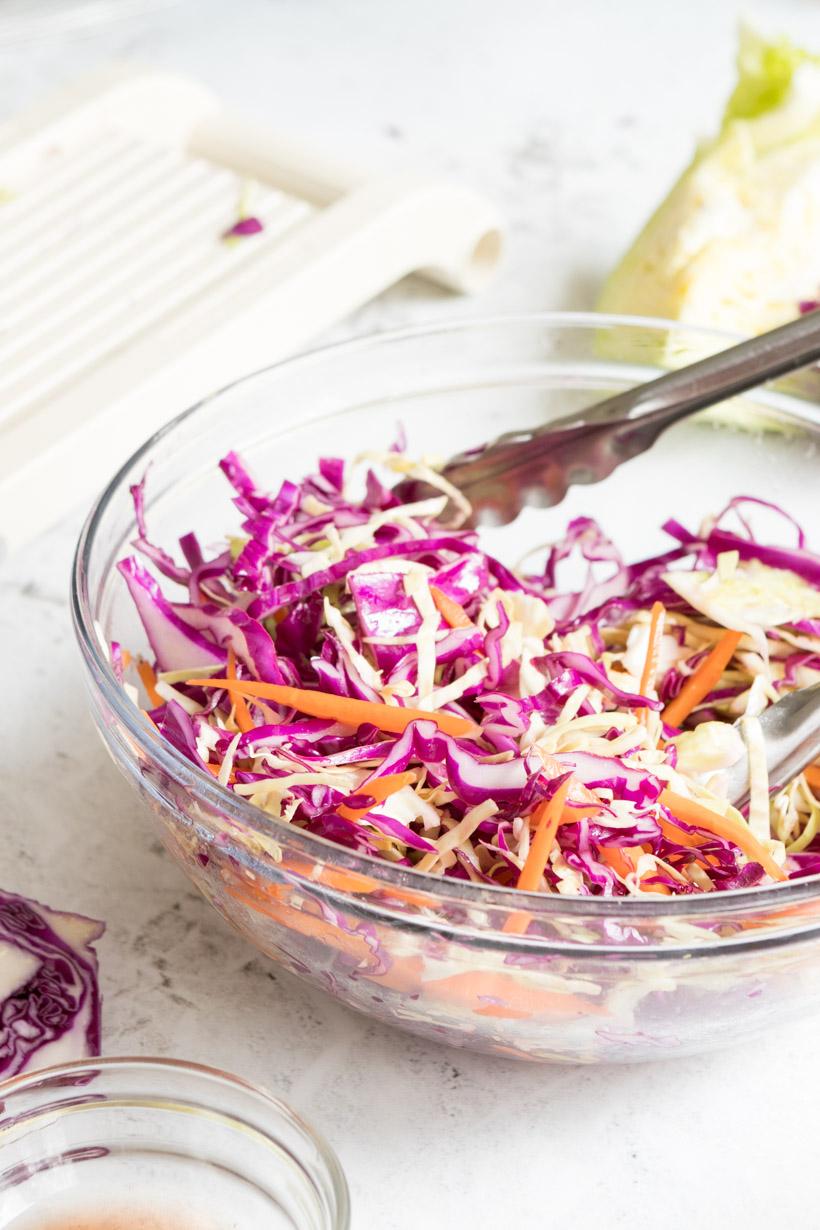 red wine vinegar coleslaw in a glass bowl with tongs in it