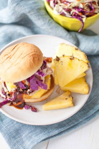 Instant Pot pulled pork sandwich on a plate with a side of pineapple