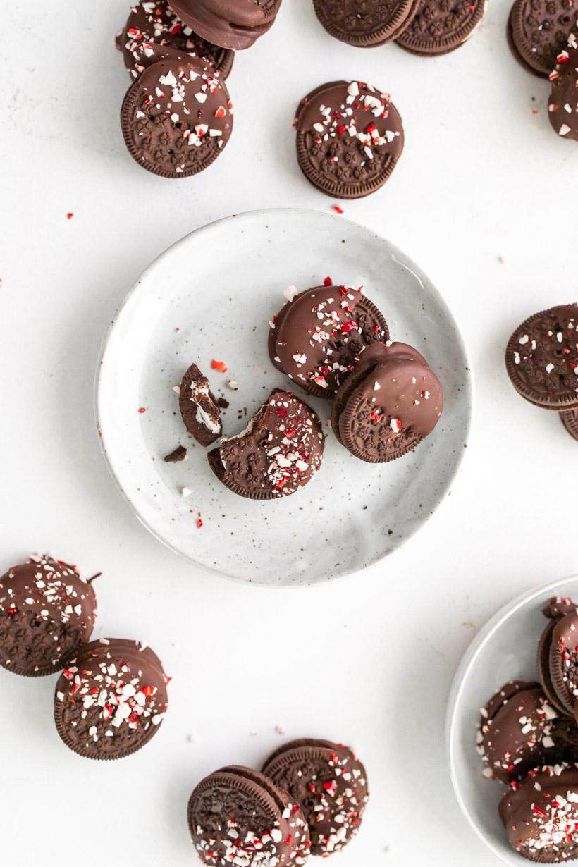 Multiple chocolate dipped oreos with peppermint on a plate and the table 