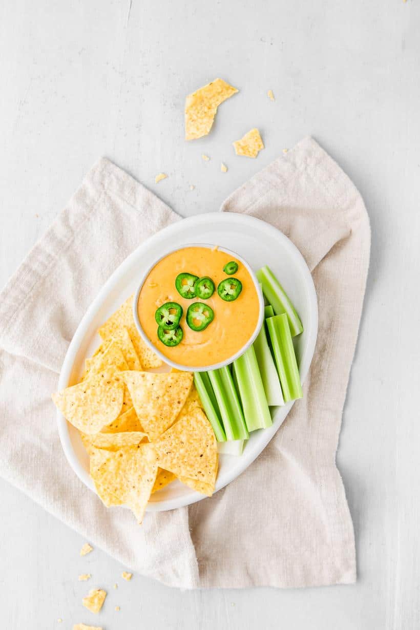 easy queso dip with sliced jalapenos on top with chips and celery on a plate
