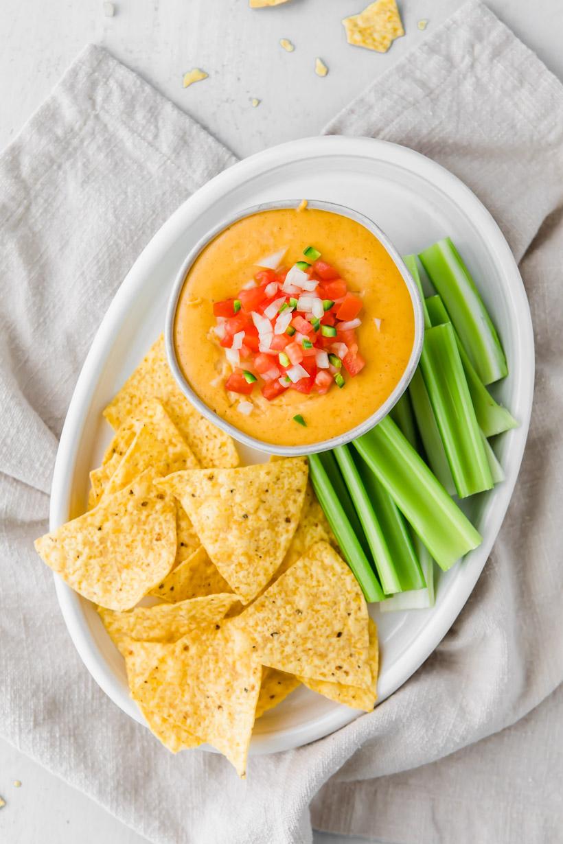 queso dip on a plate with salsa on top and chips and celery on the side