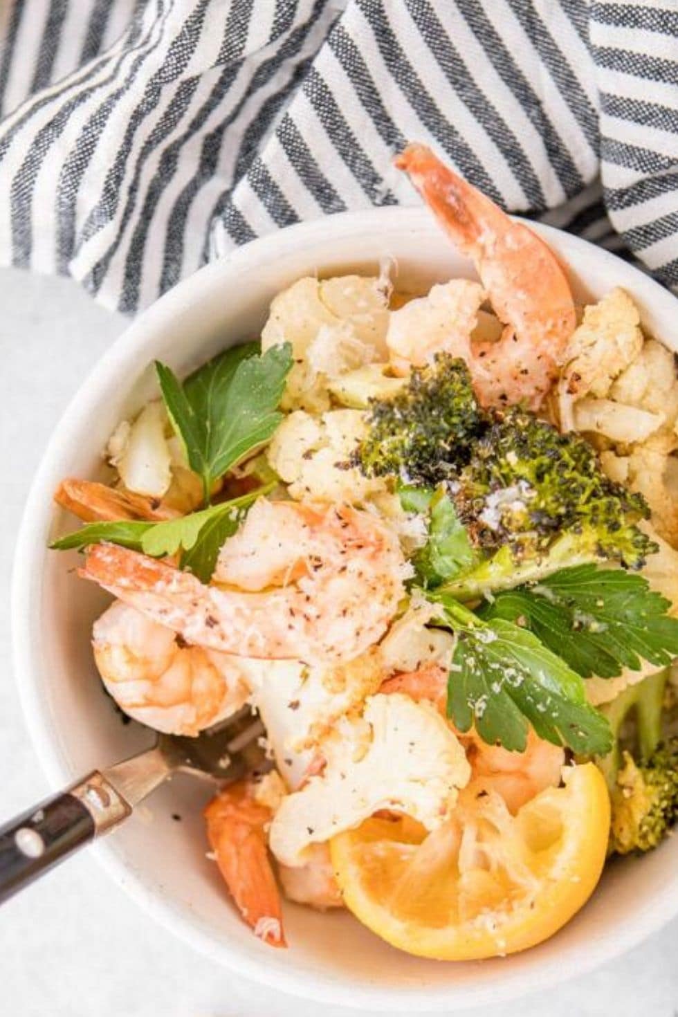 close up of shrimp, vegetables and lemons in a white bowl