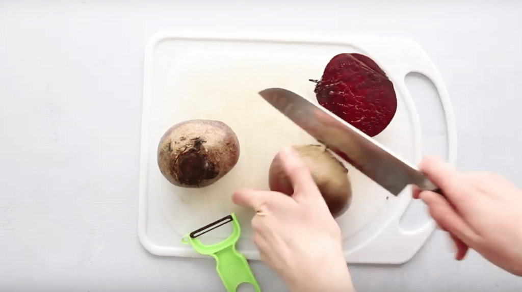 two hands cutting the end off a beet with a chefs knife