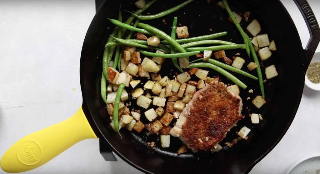pan seared pork chop with green beans potatoes cooking on a cast iron skillet