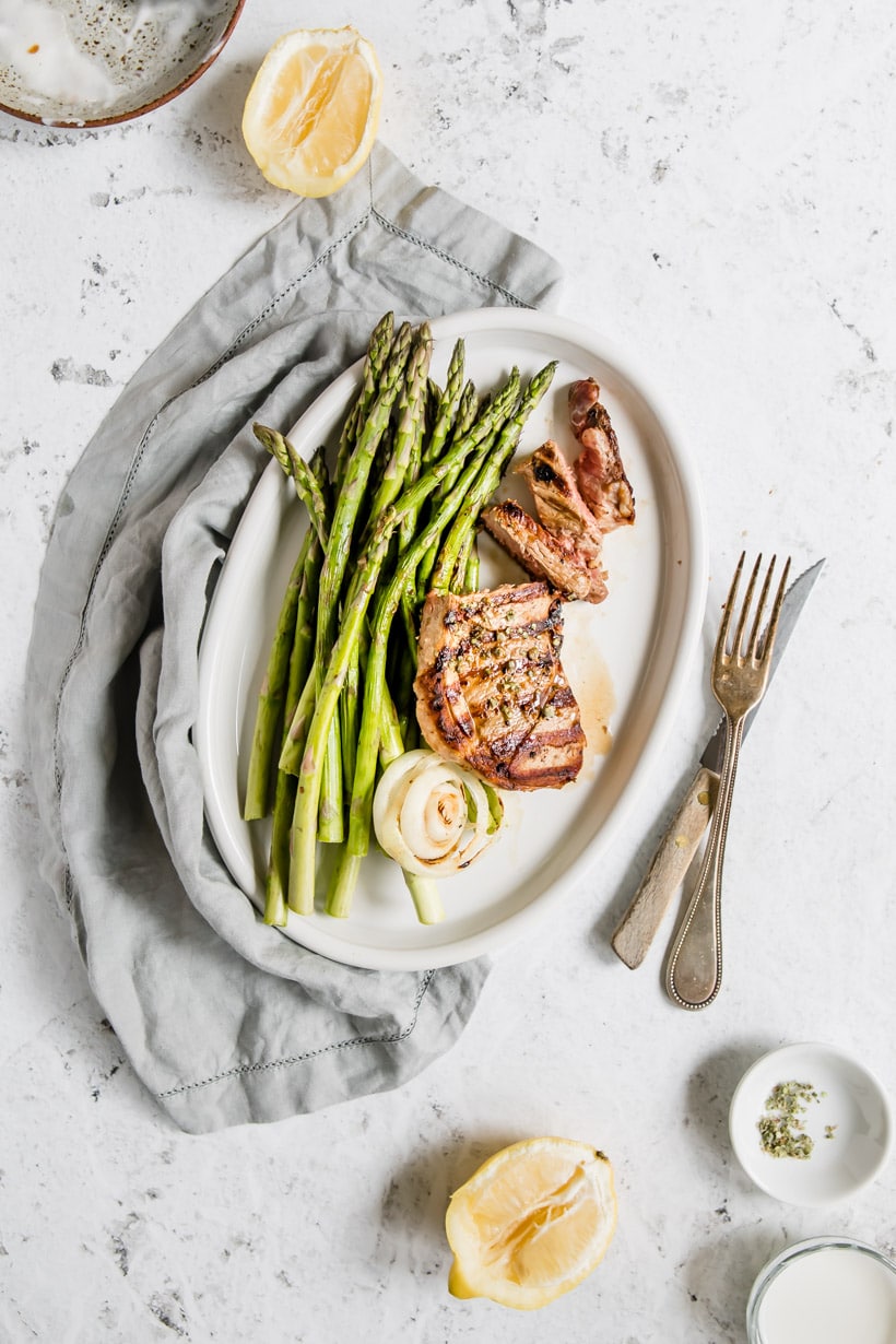 sliced lamb steak with asparagus on a plate with ingredients on table