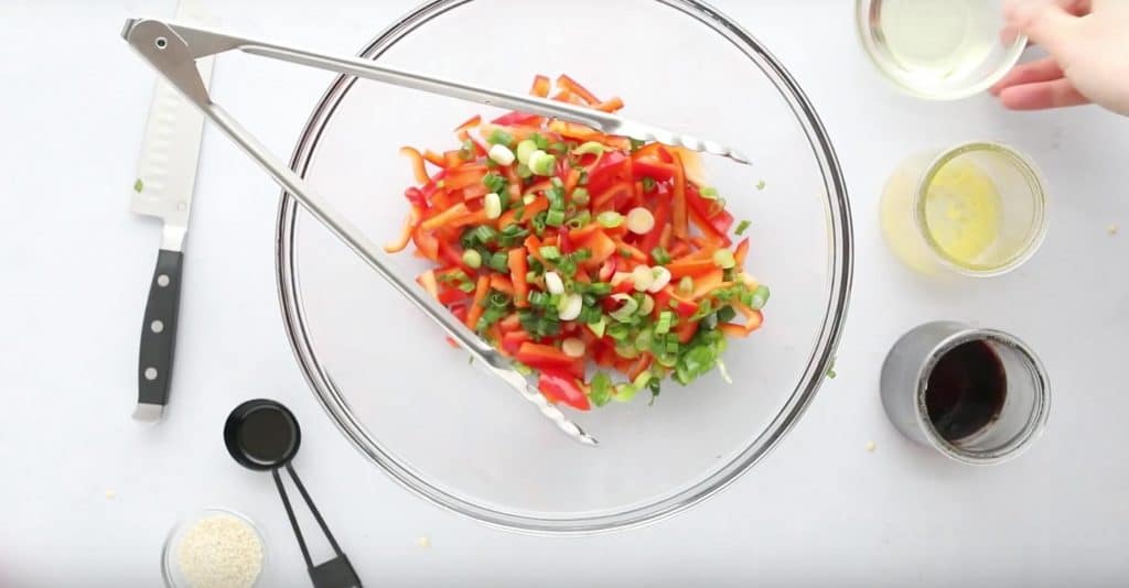 red bell peppers and green onions in a bowl with sauces on the side