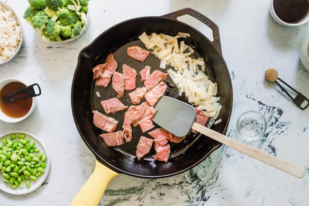 sliced beef and onions cooking in a cast iron skillet