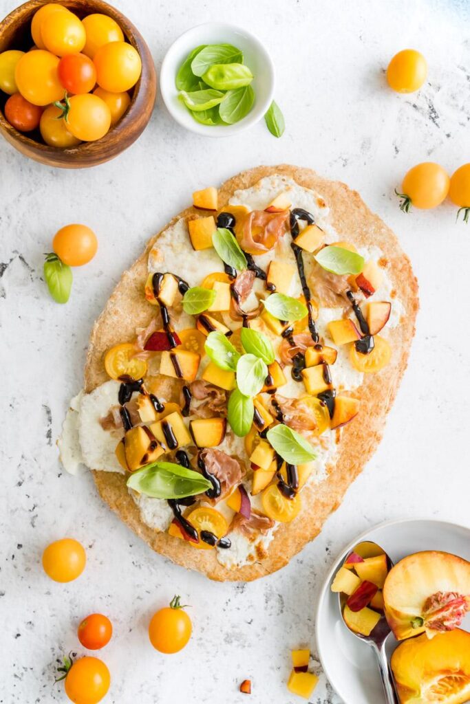 peach and prosciutto pizza caprese with ingredients on a table