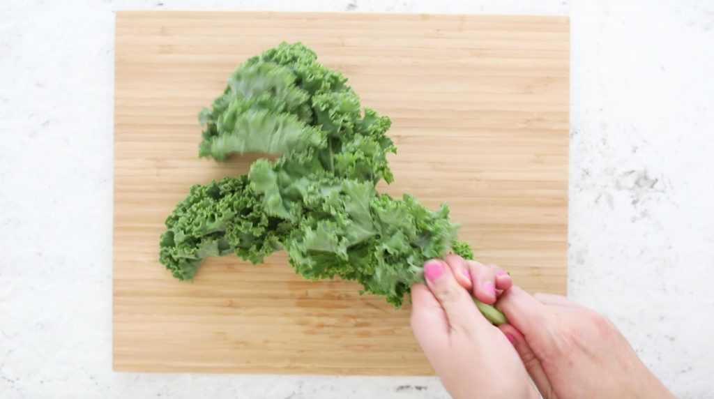 hands removing kale leaves from the stalks