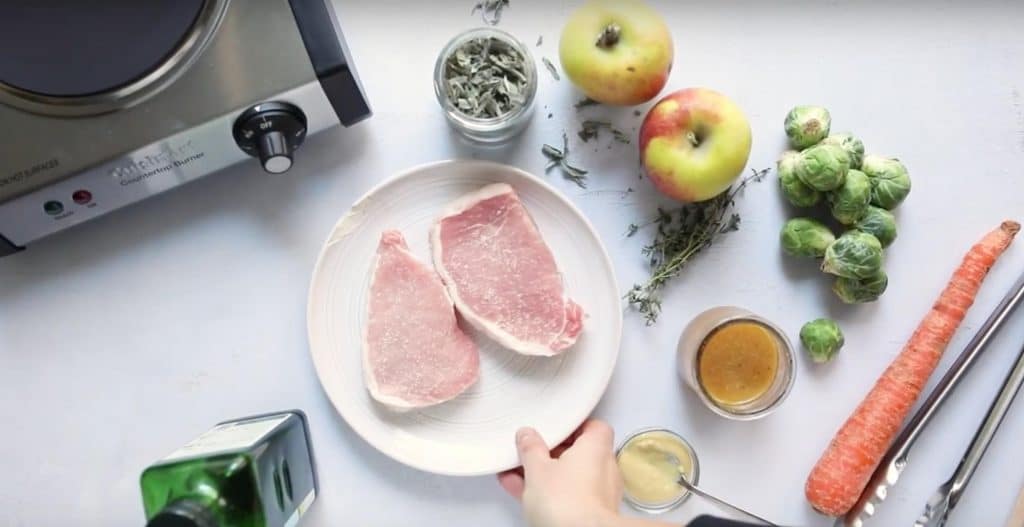 ingredients for pan fried pork chops with apples and vegetables on a table