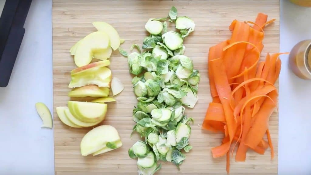 sliced apples, brussels sprouts, and carrot ribbons on a cutting board