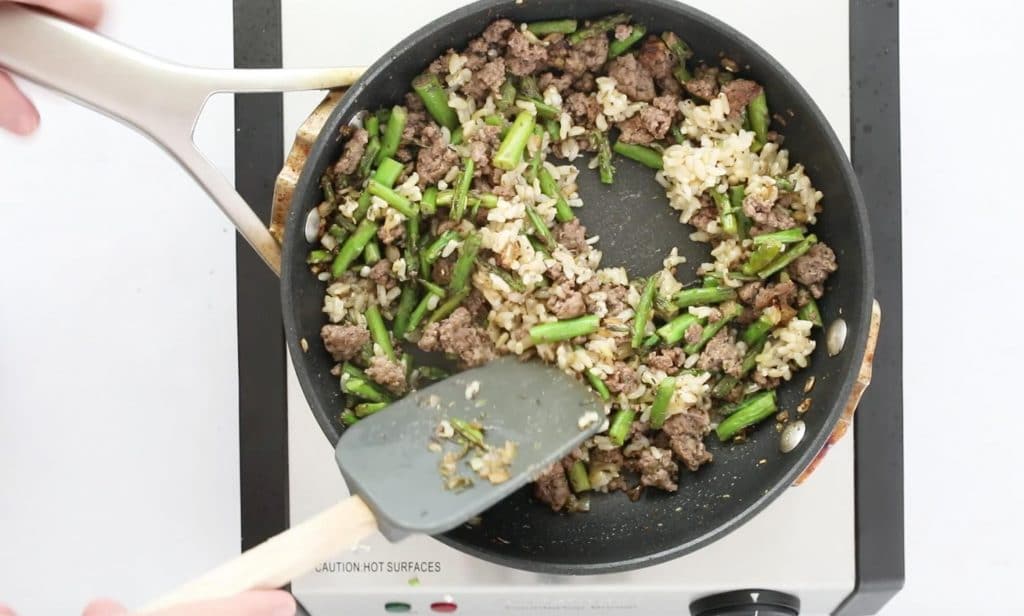 mixing ground beef, vegetables, and rice in sautee pan