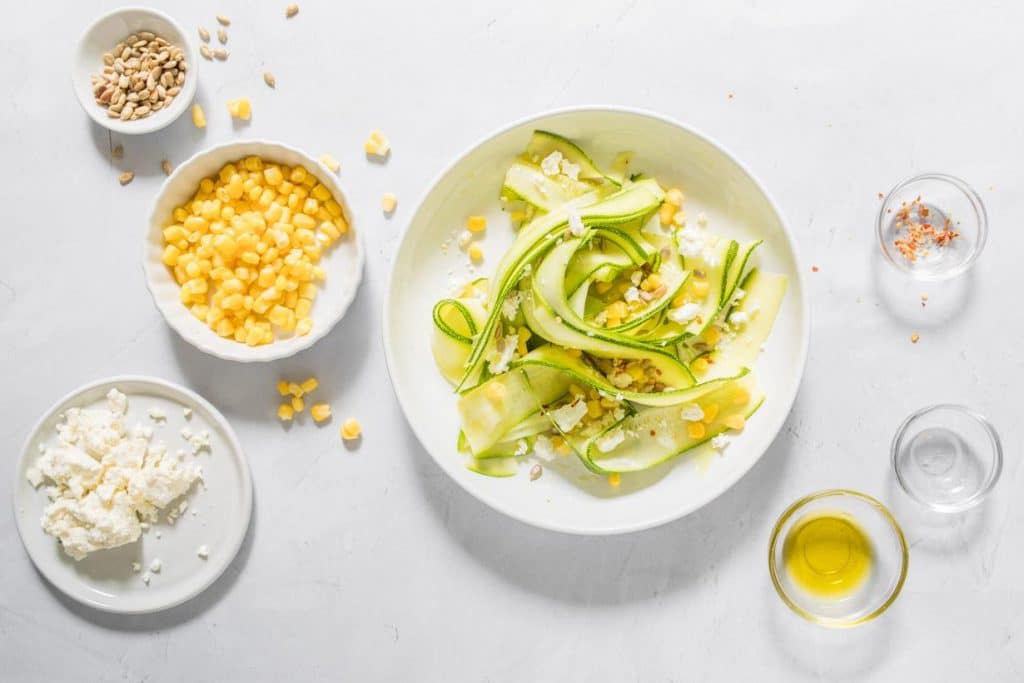 zucchini salad with feta on a table with ingredients next to it