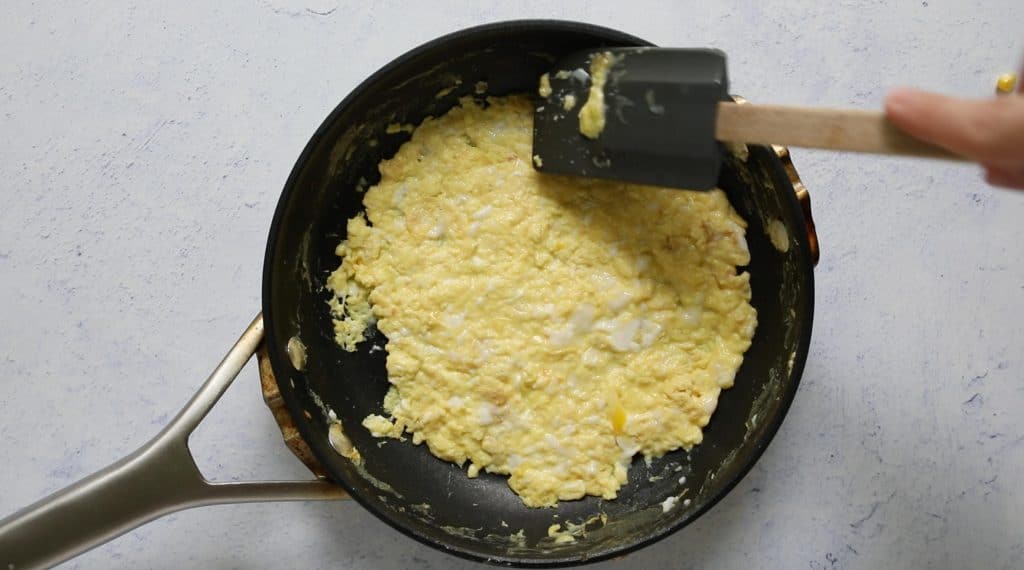 pressing down eggs with a spatula in a fry pan
