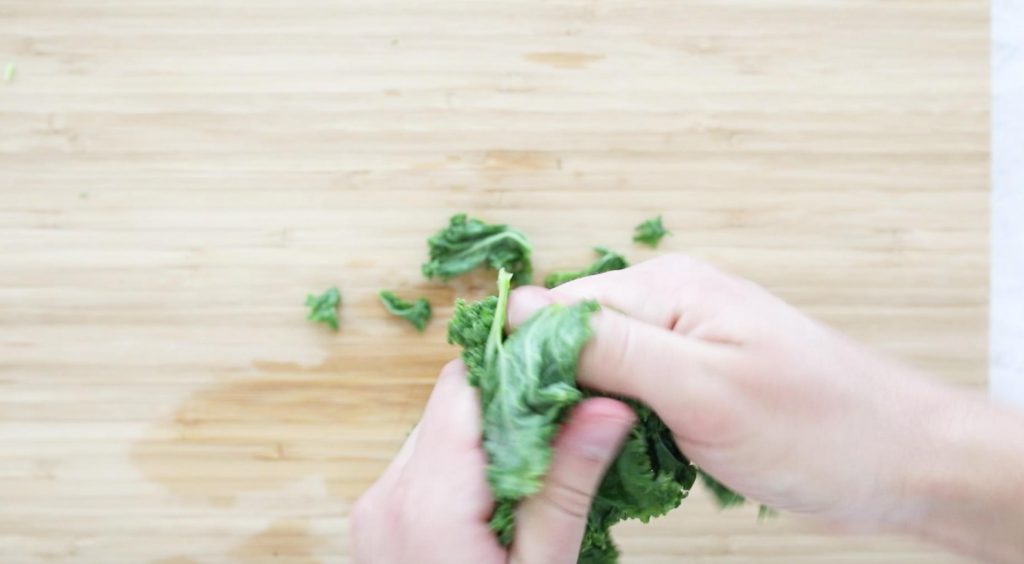 hands massaging kale over a cutting board
