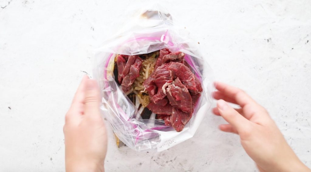 hands holding a plastic bag full of beef with marinade ingredients in it