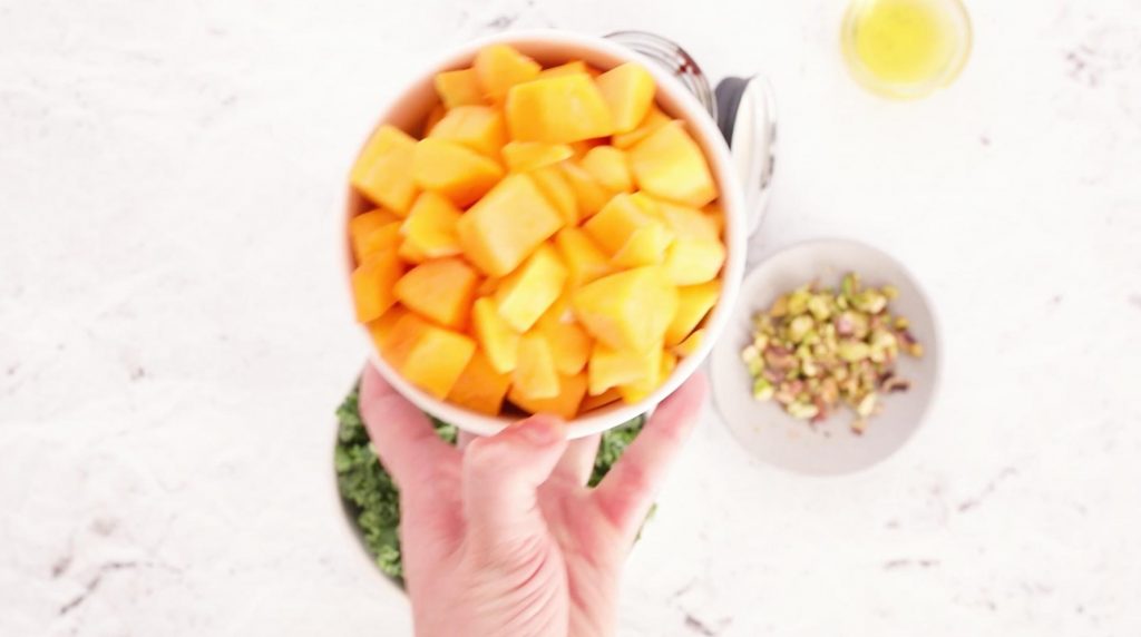 hand holding a white bowl of cubed butternut squash with other salad ingredients below 