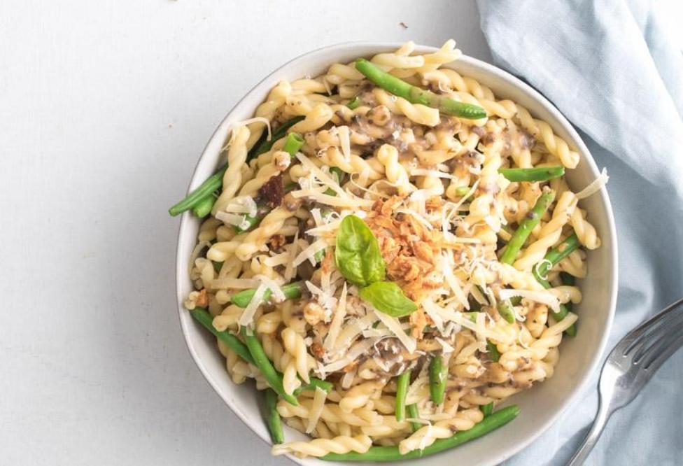 bowl of pasta with mushroom sauce and green beans with cheese and basil leaves on top