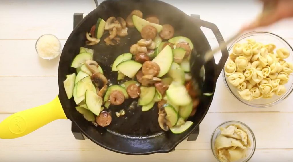 sliced sausage, mushrooms, and zucchini cooking in a cast iron skillet