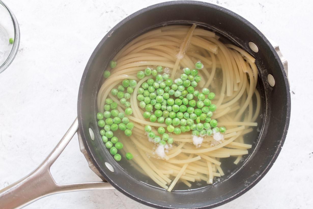 pasta and peas cooking in water in a black pot