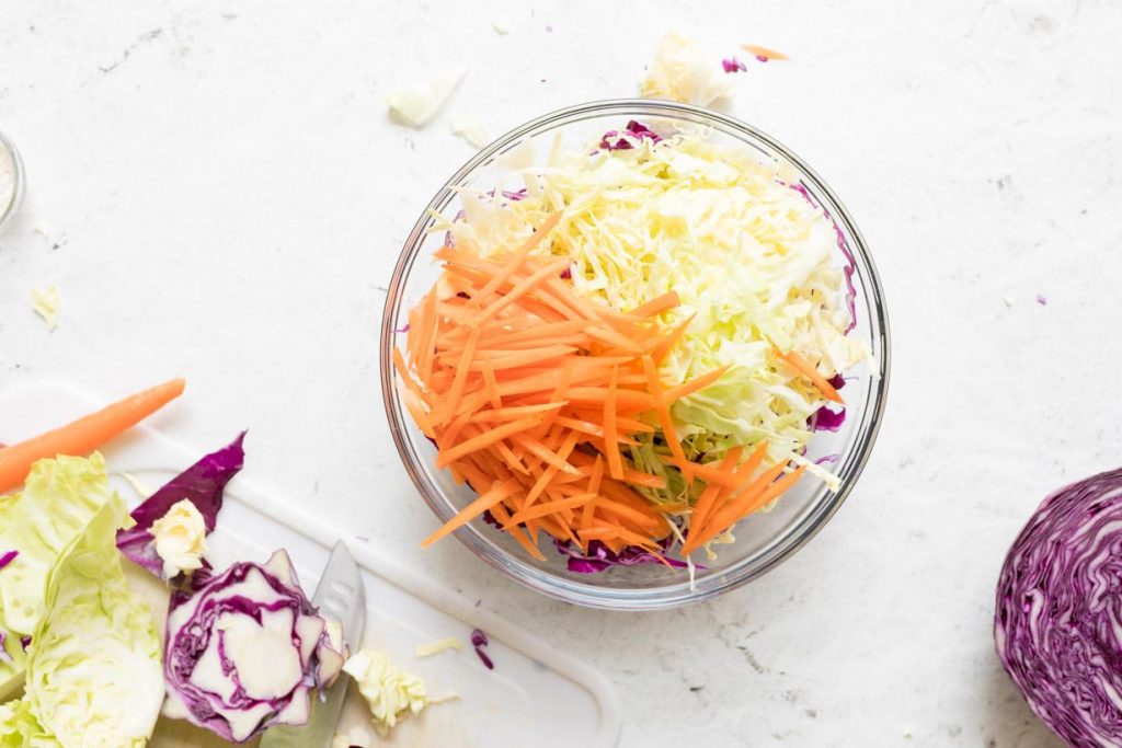 shredded cabbage and carrots in a glass bowl with ingredients next to it