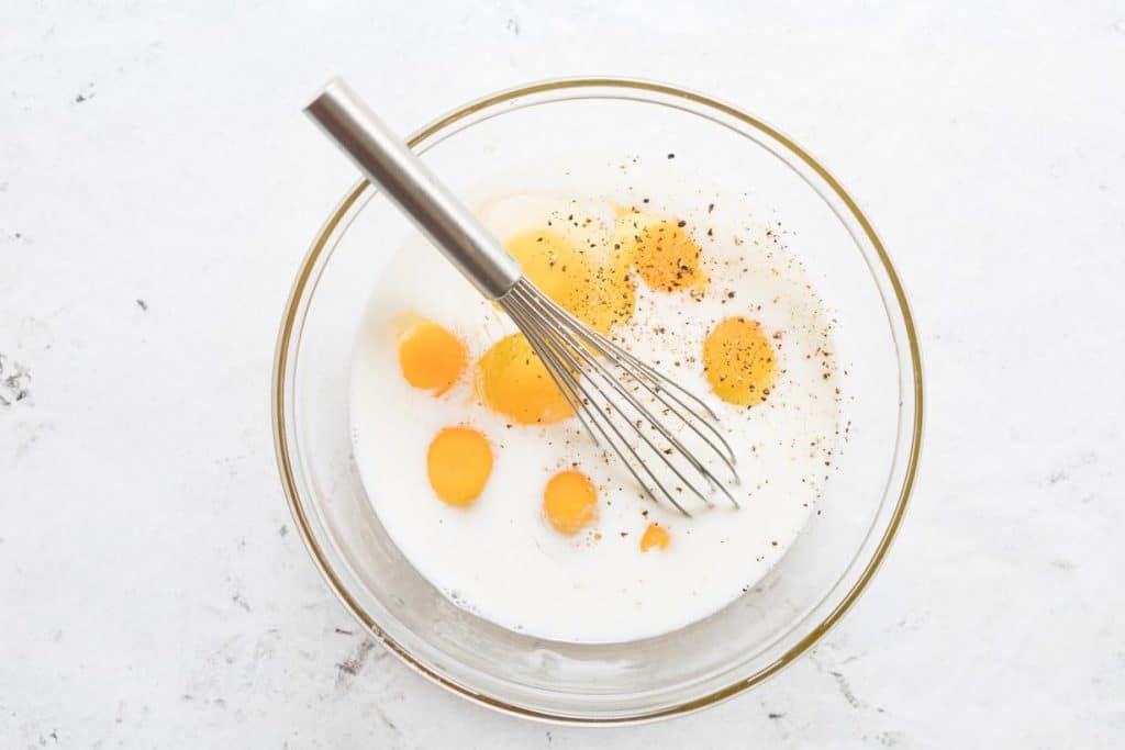 eggs and milk in a glass bowl with a whisk in it