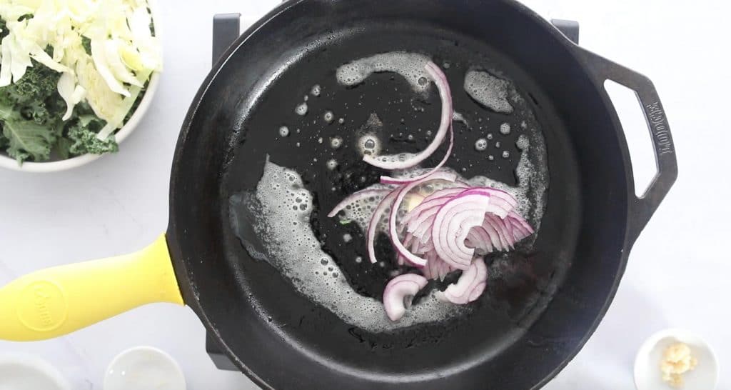 sliced red onions and butter cooking in a cast iron skillet