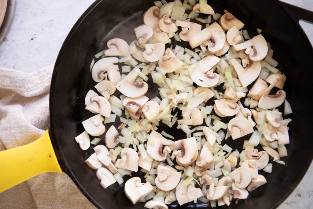 raw mushrooms and onions in a cast iron skillet