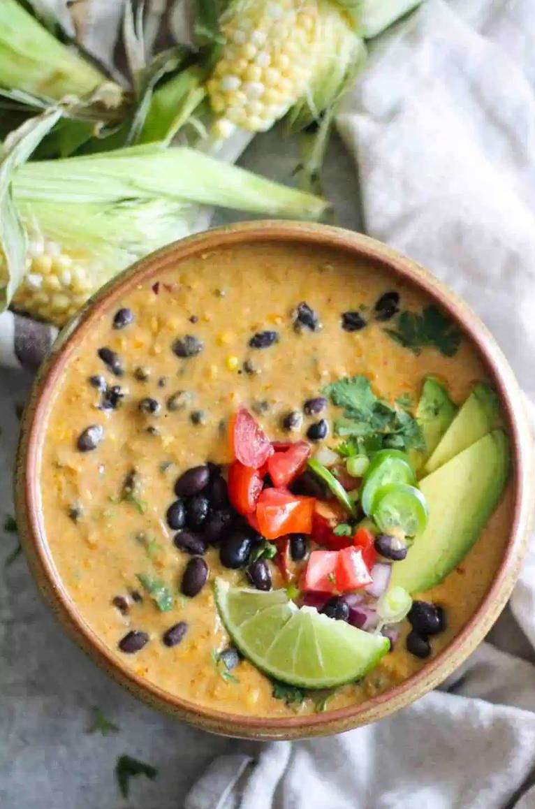 vegan corn chowder with tomatoes, black beans, a lime, and avocado on top